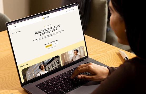 A young woman looks at her laptop sitting at a desk. The screen shows a webpage.